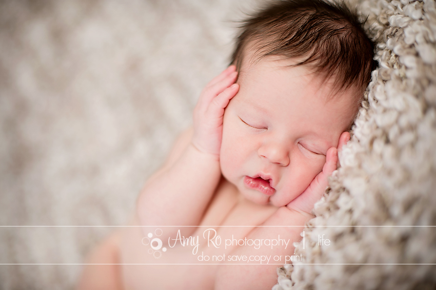 Sleeping newborn with hands on cheeks on a brown blanket