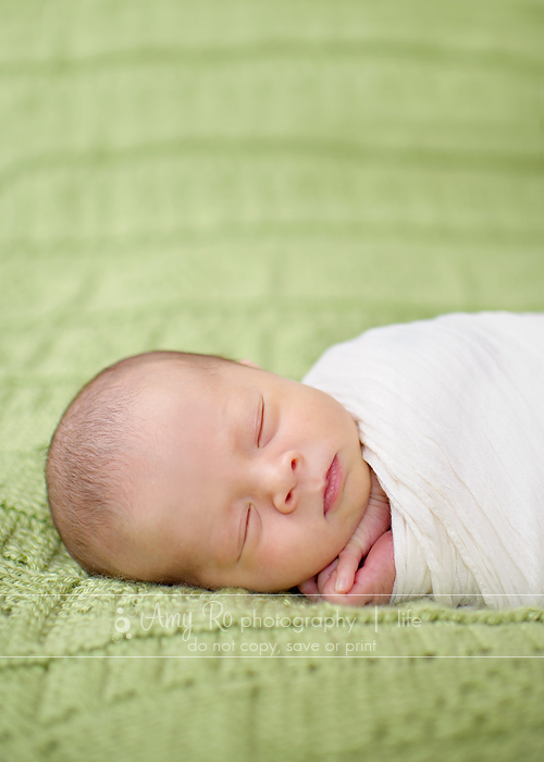 Newborn baby on green blanket swaddled