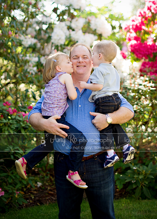 Kids kissing dad, family in front of flowers