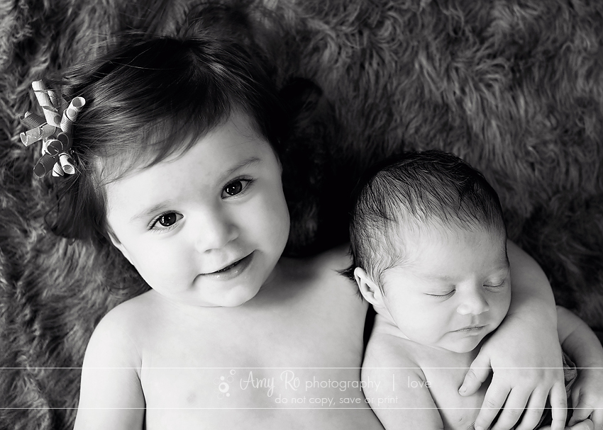 Black and white big sister with newborn image, fur rug