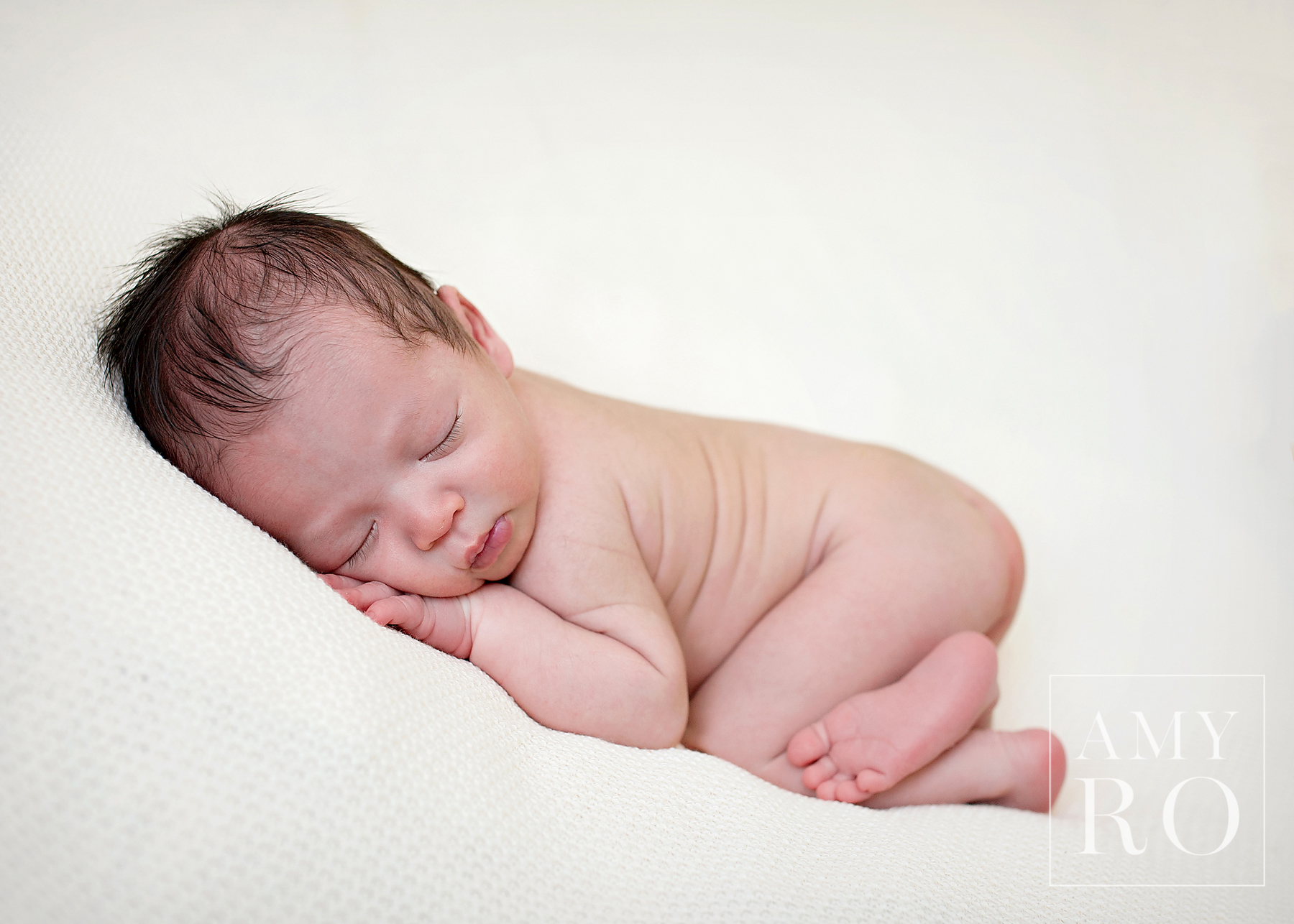 Image of newborn baby boy on cream blanket sleeping curled up during a newborn session Rhode Island Newborn photographer Amy Ro