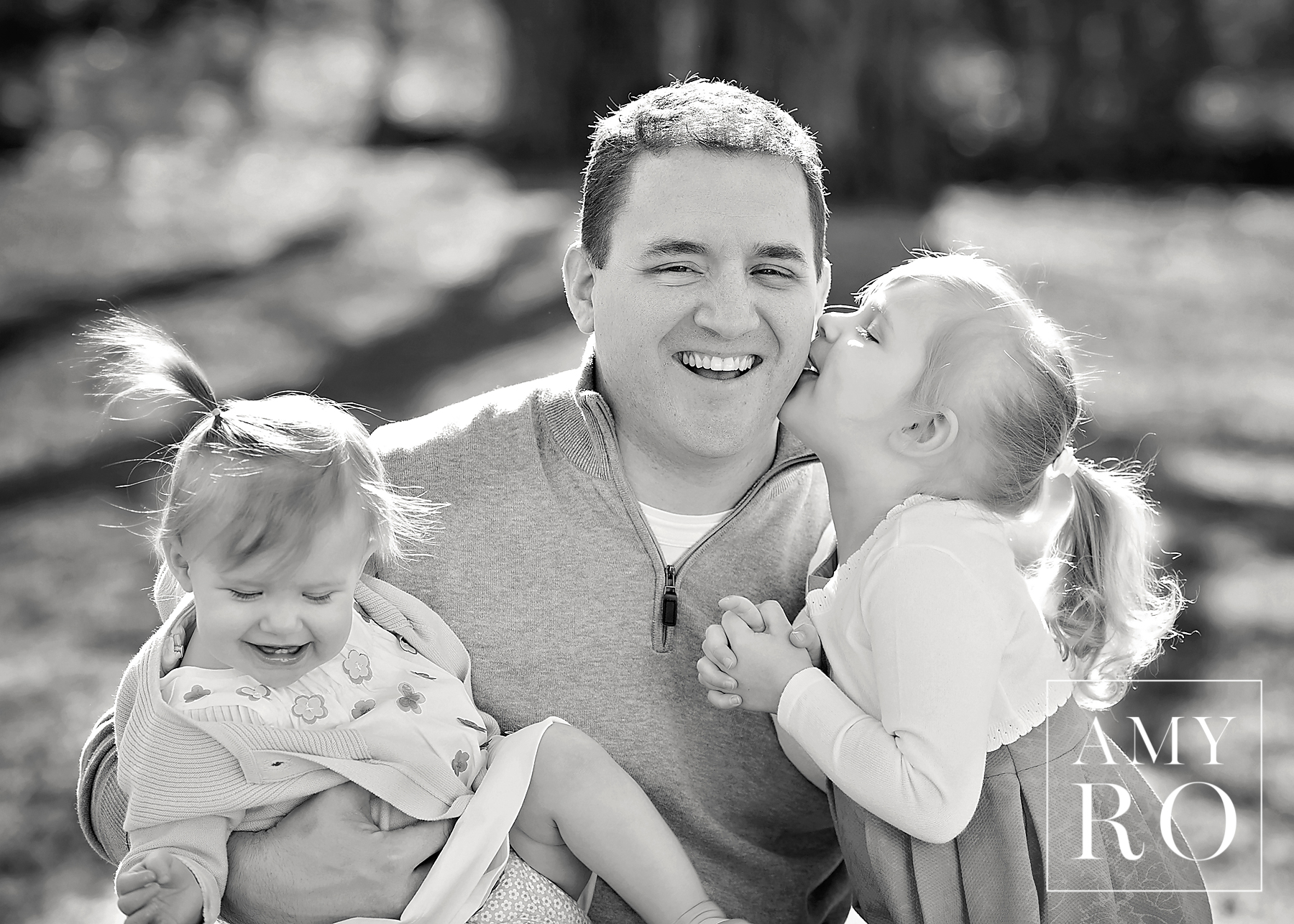Black and white image of dad with his daughters getting kisses during a family lifestyle session in Massachusetts