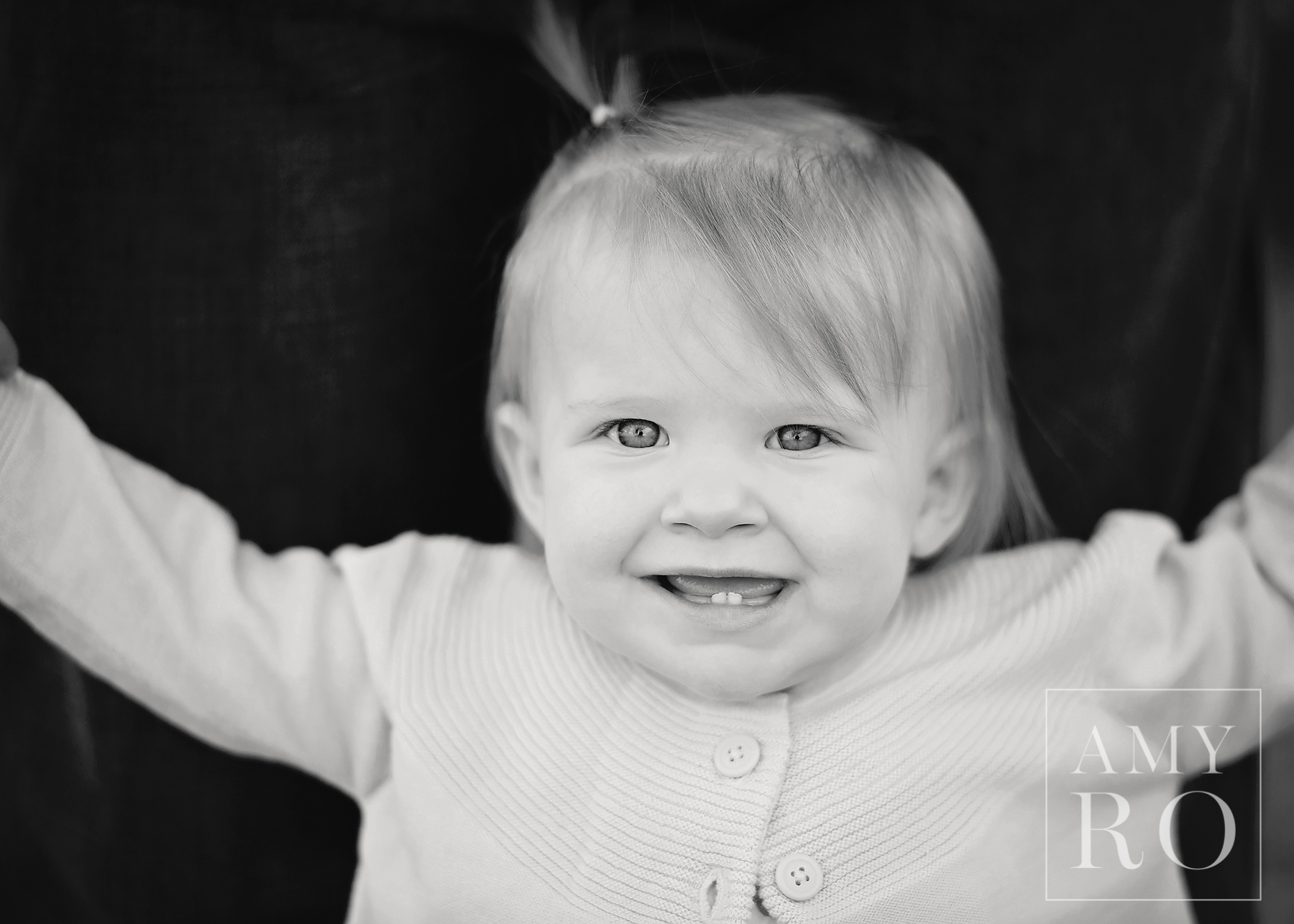 Black and white image of baby girl smiling with her two bottom teeth showing
