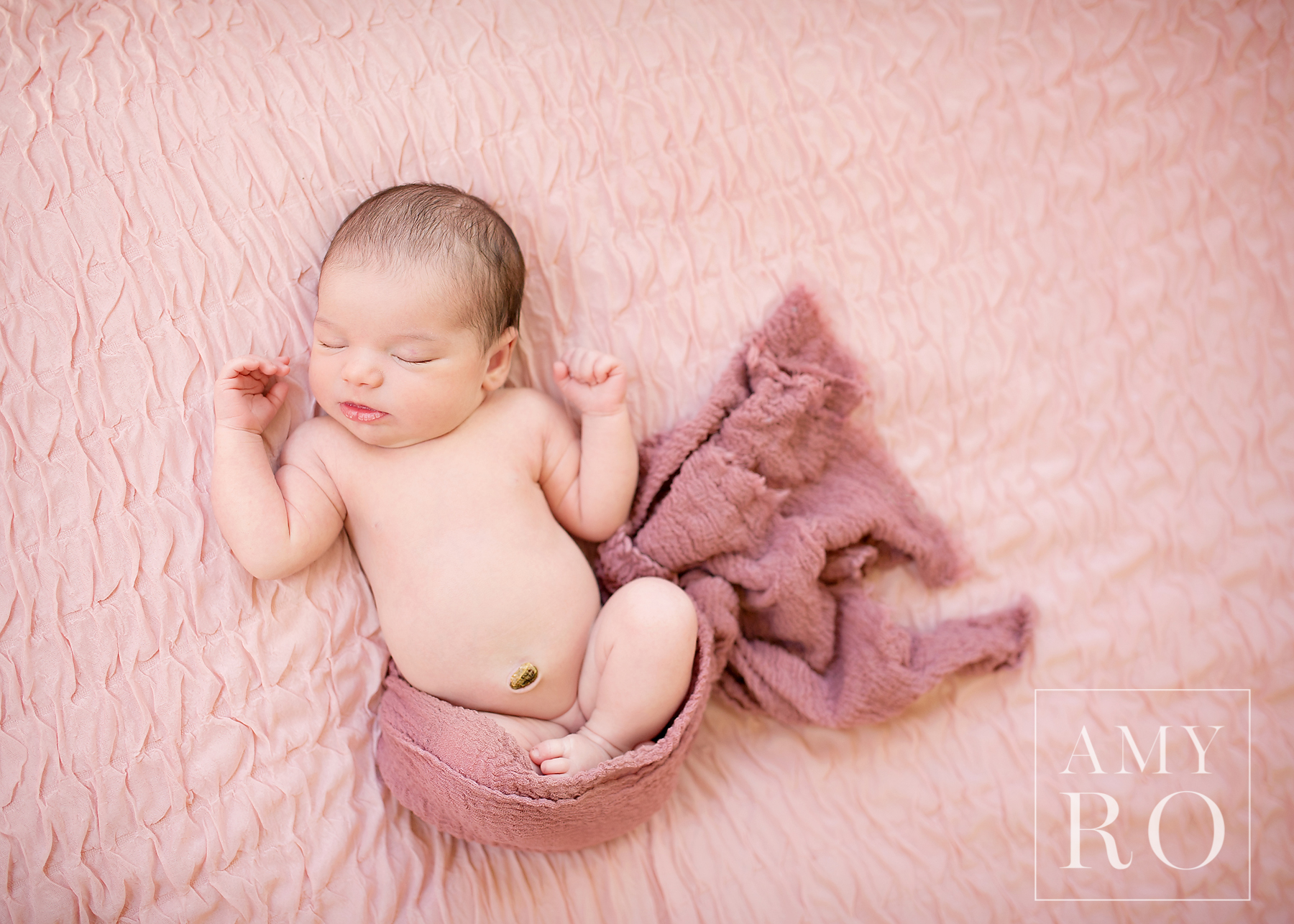 Overhead shot of newborn baby girl on pink backdrop with pink swaddle sleeping during a newborn session in Rhode Island