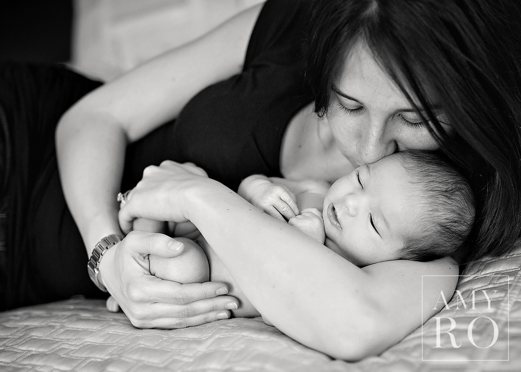 Black and white image of mom snuggling newborn baby on the bed taken during an in-home newborn photography session in Rhode Island