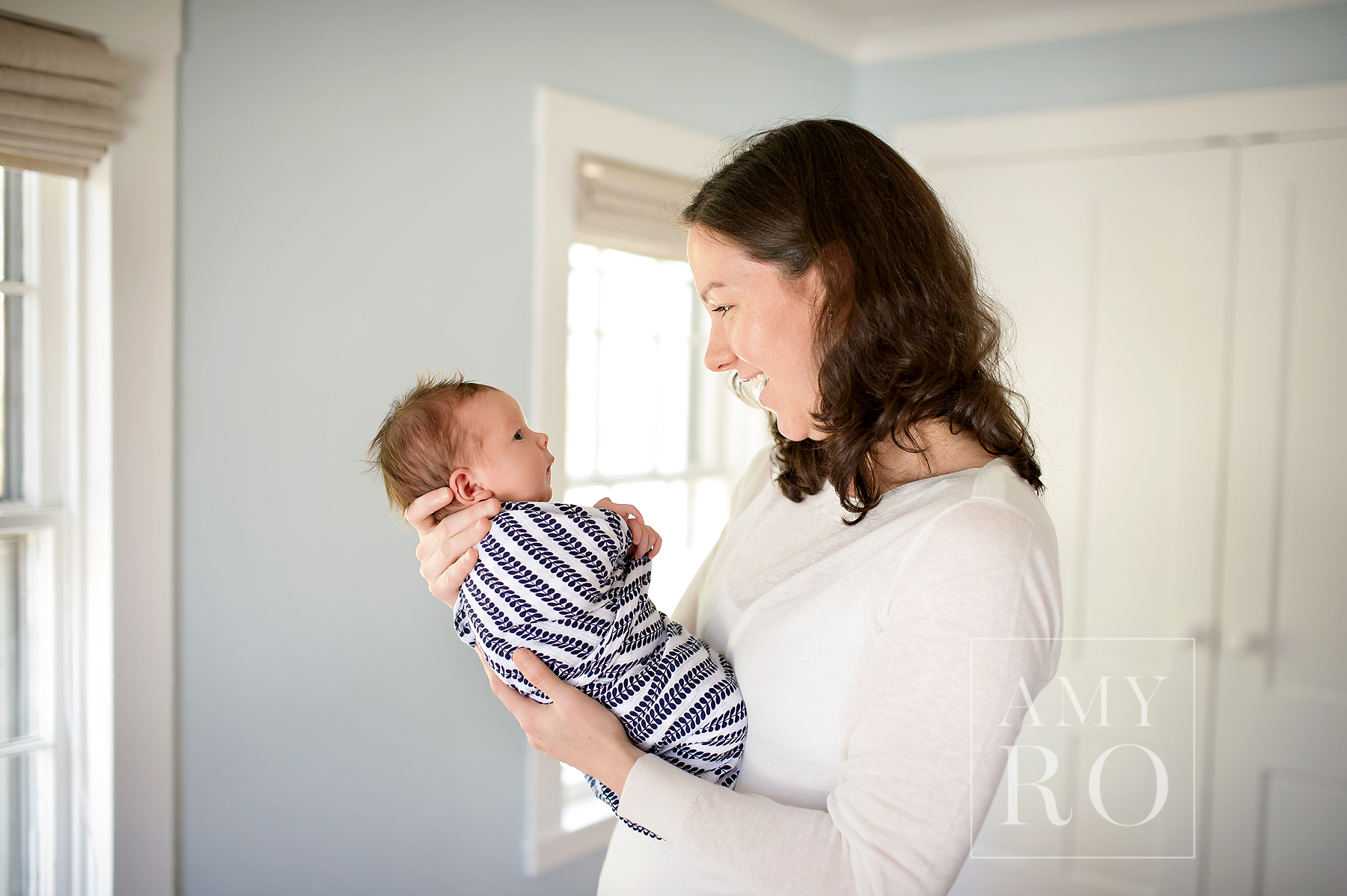 Mom looking at baby smiling during a newborn session in their bedroom in Massachusetts