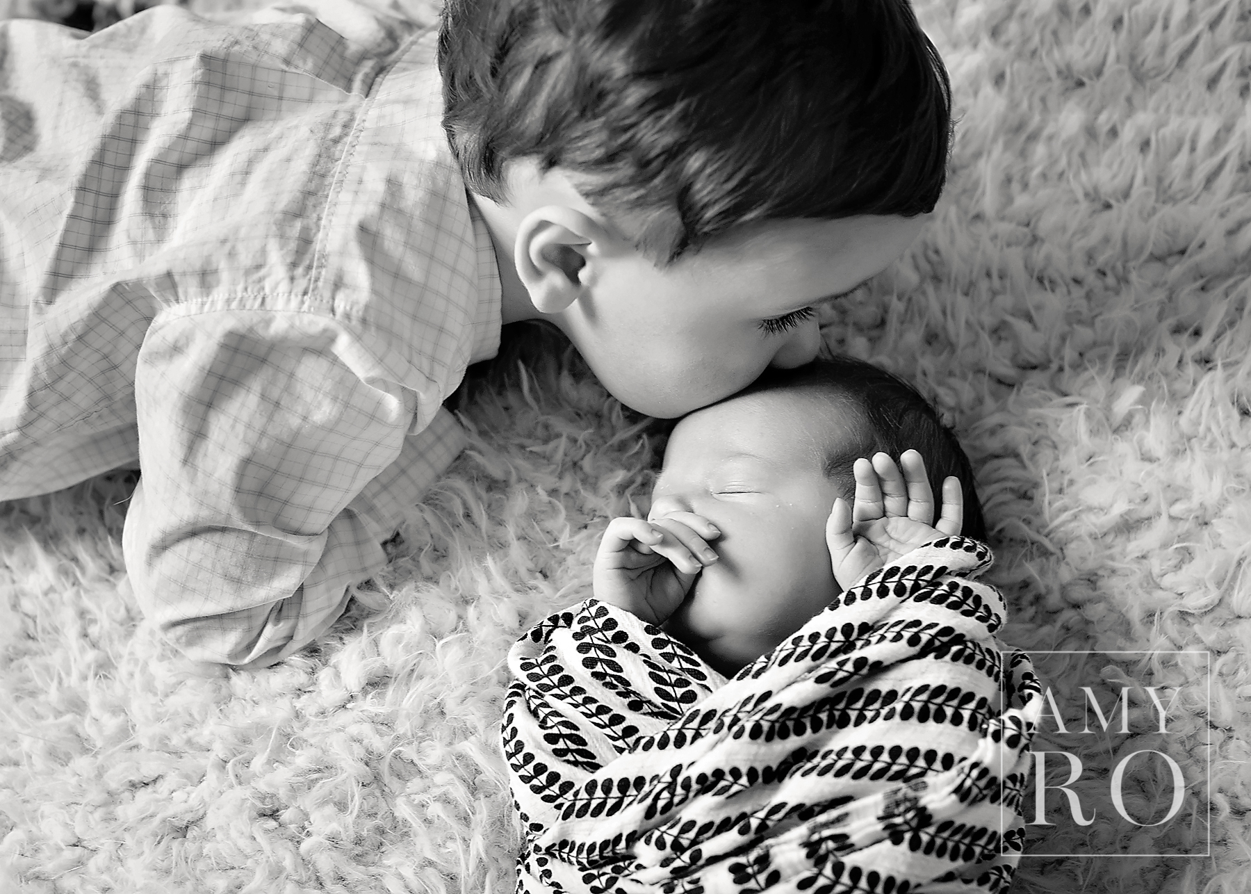 Black and white image of toddler kissing newborn sister during photography session in Massachusetts