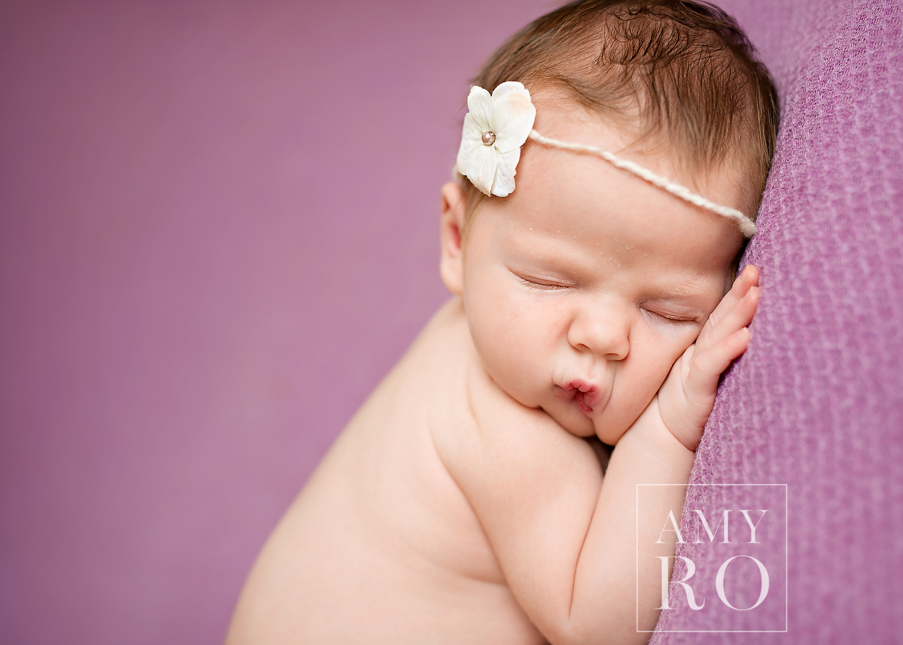 Sleeping image of newborn girl with flower headband on a purple blanket taken during newborn session photography in Massachusetts