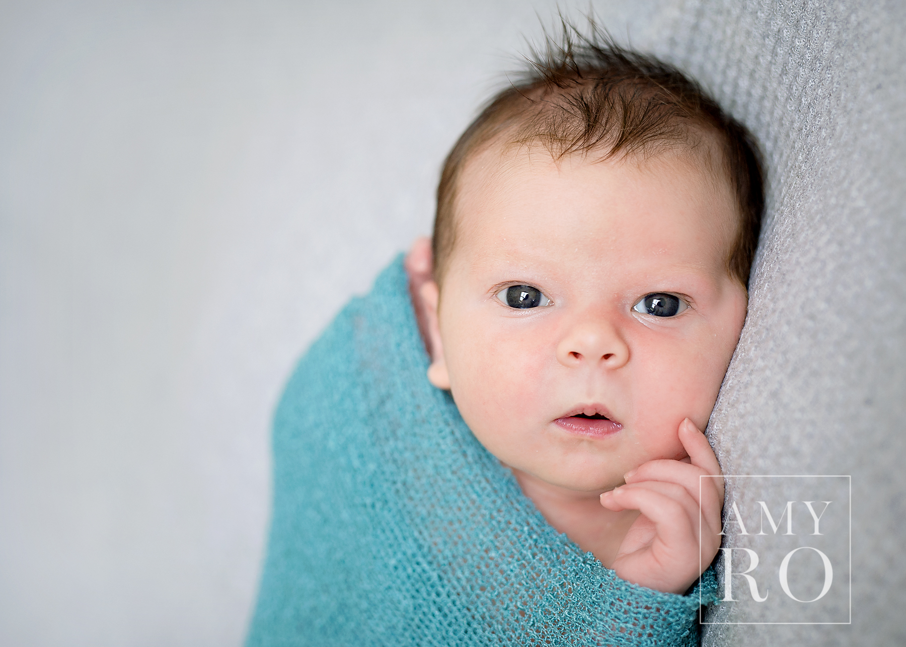 Color image of awake newborn girl in teal swaddle on a grey blanket