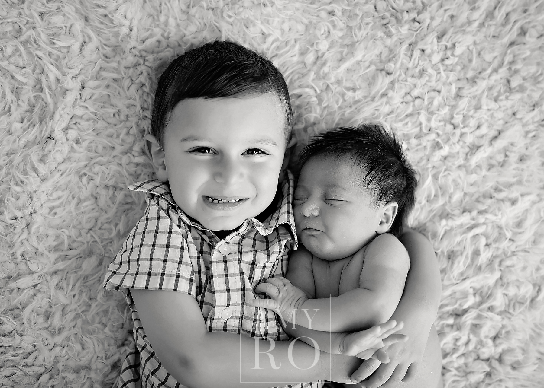 Black and white image of brother snuggling with his newborn sister during a lifestyle newborn session
