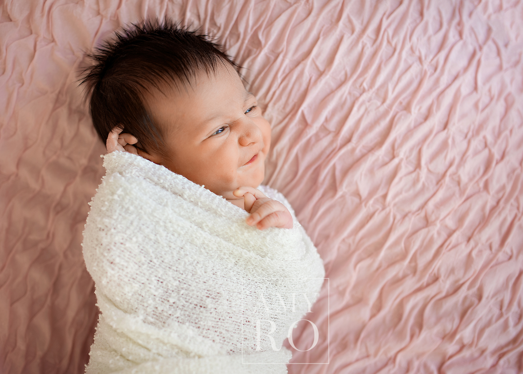 Newborn baby girl swaddled in ivory on a pink blanket smiling during newborn session near Massachusetts