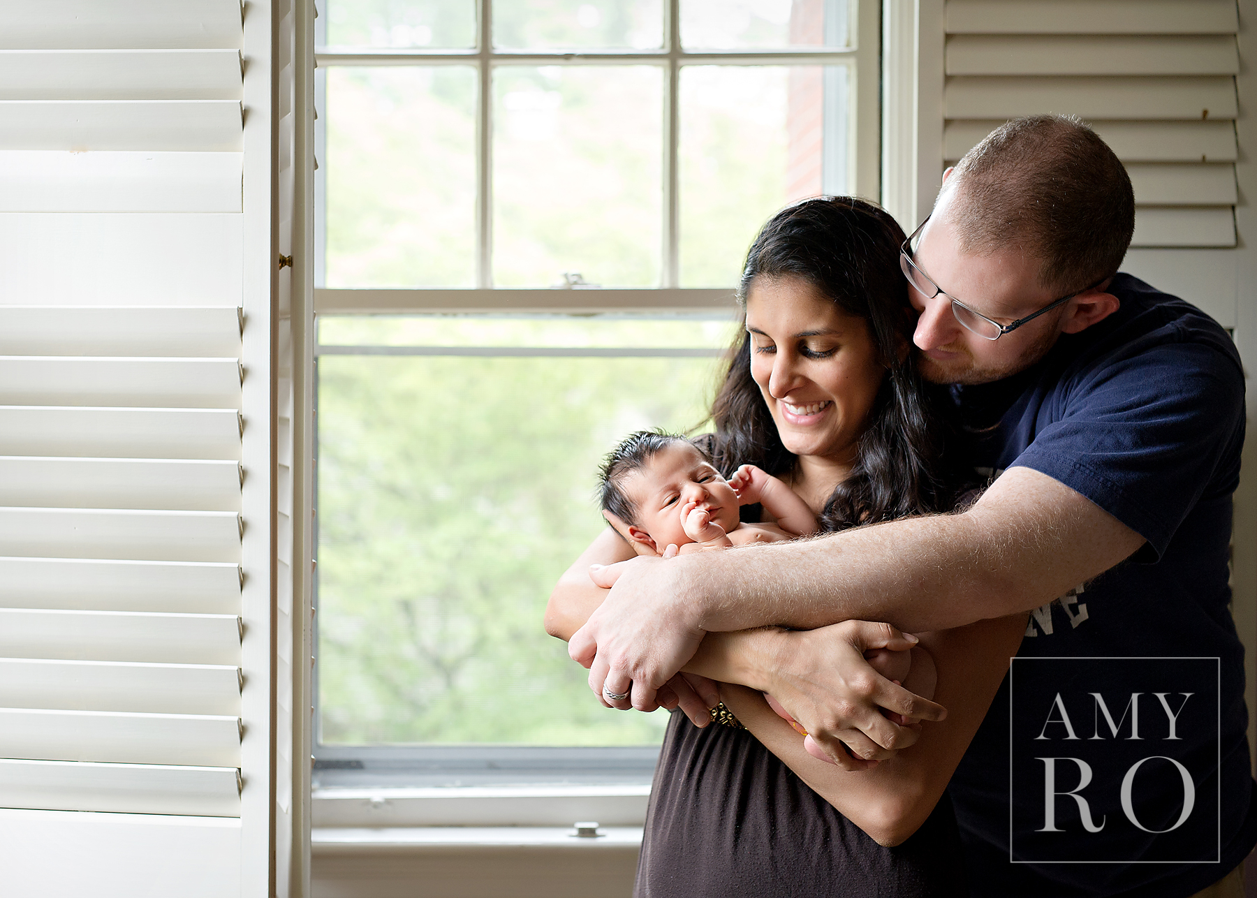 Image of mom and dad snuggling newborn baby girl in front of shuttered windows