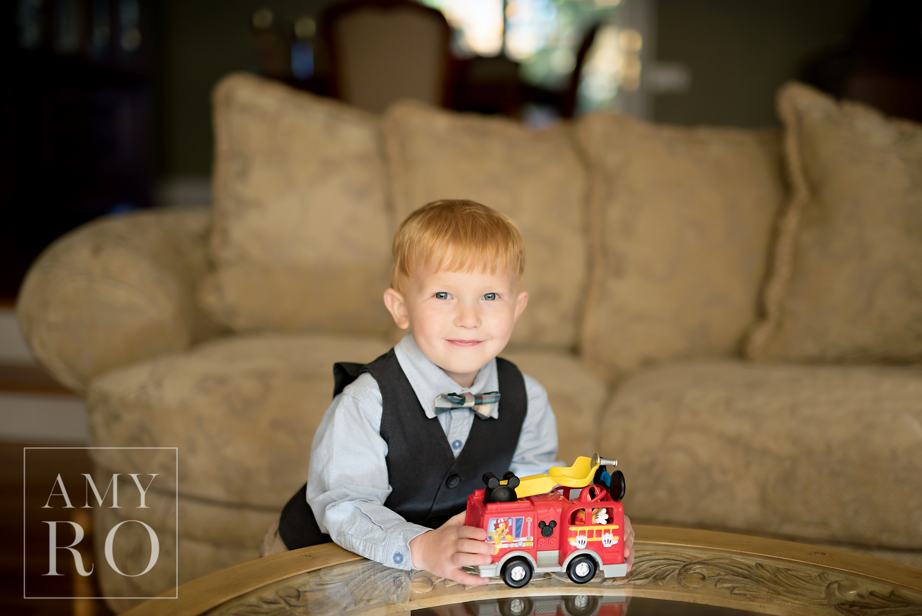 Red haired toddler in bow tie playing in his living room during a family photography session in Rhode Island