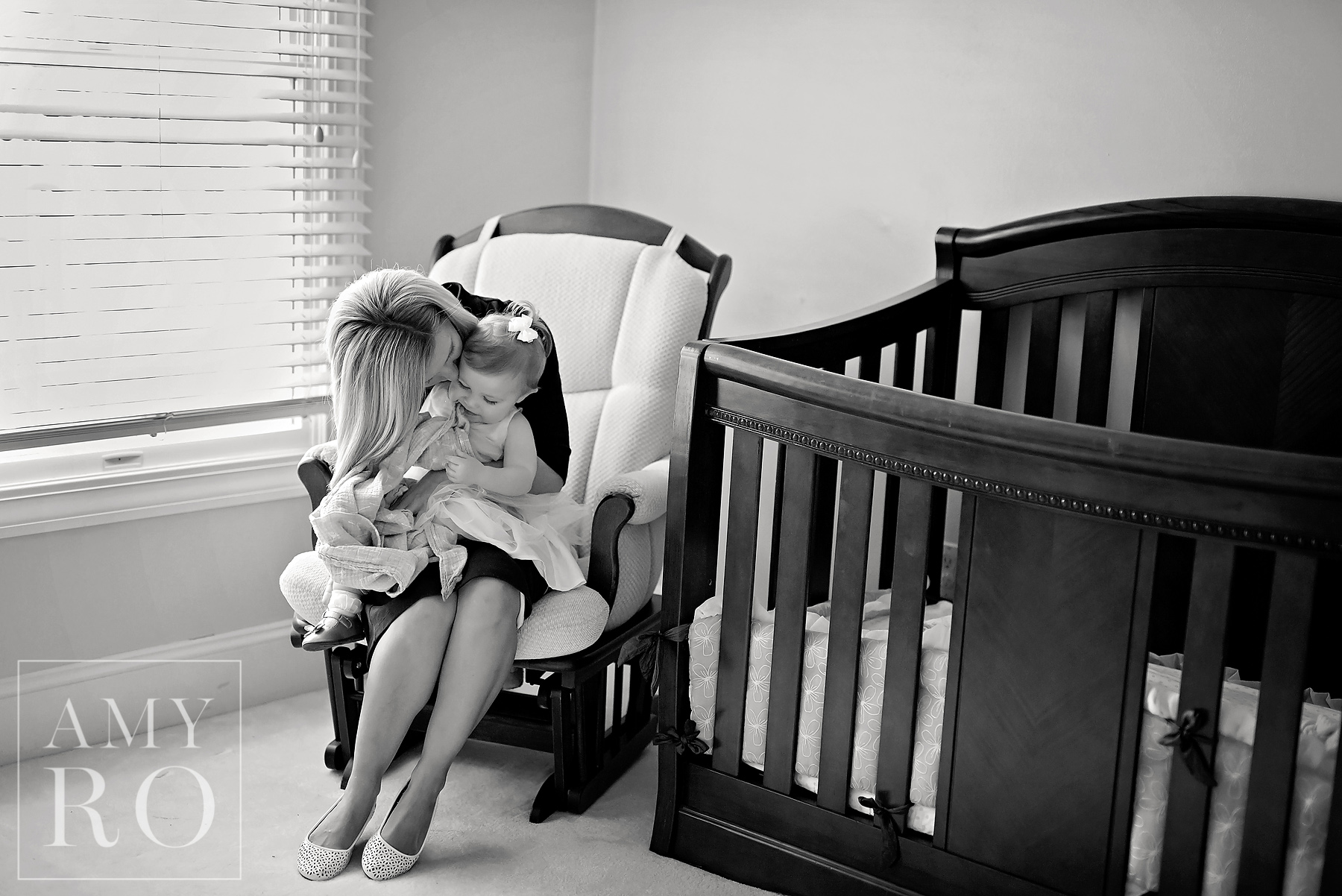 Black and white image of mom snuggling baby girl in rocking chair before nap time during lifestyle family session photography in Rhode Island