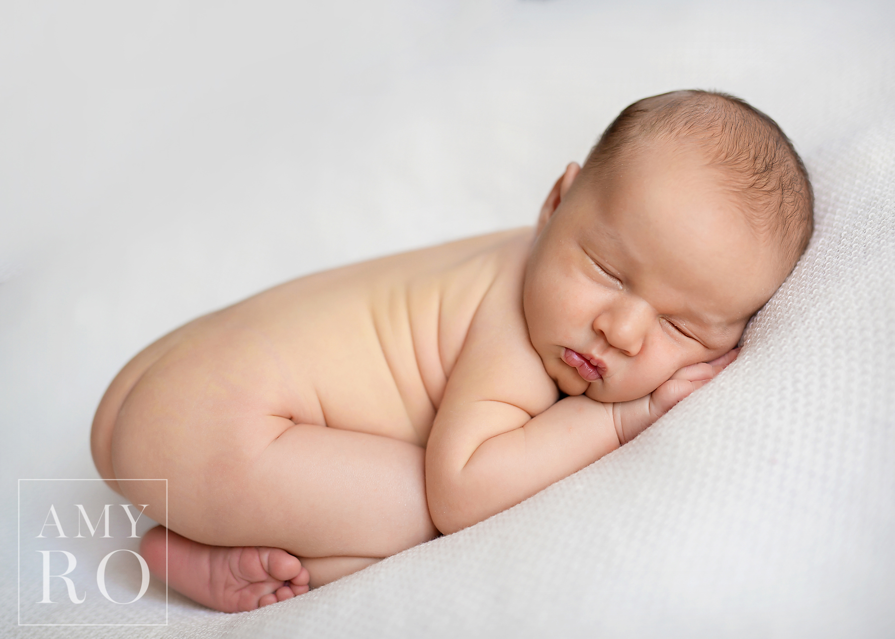 Image of sleeping newborn curled on white blanket during a newborn session in Rhode Island