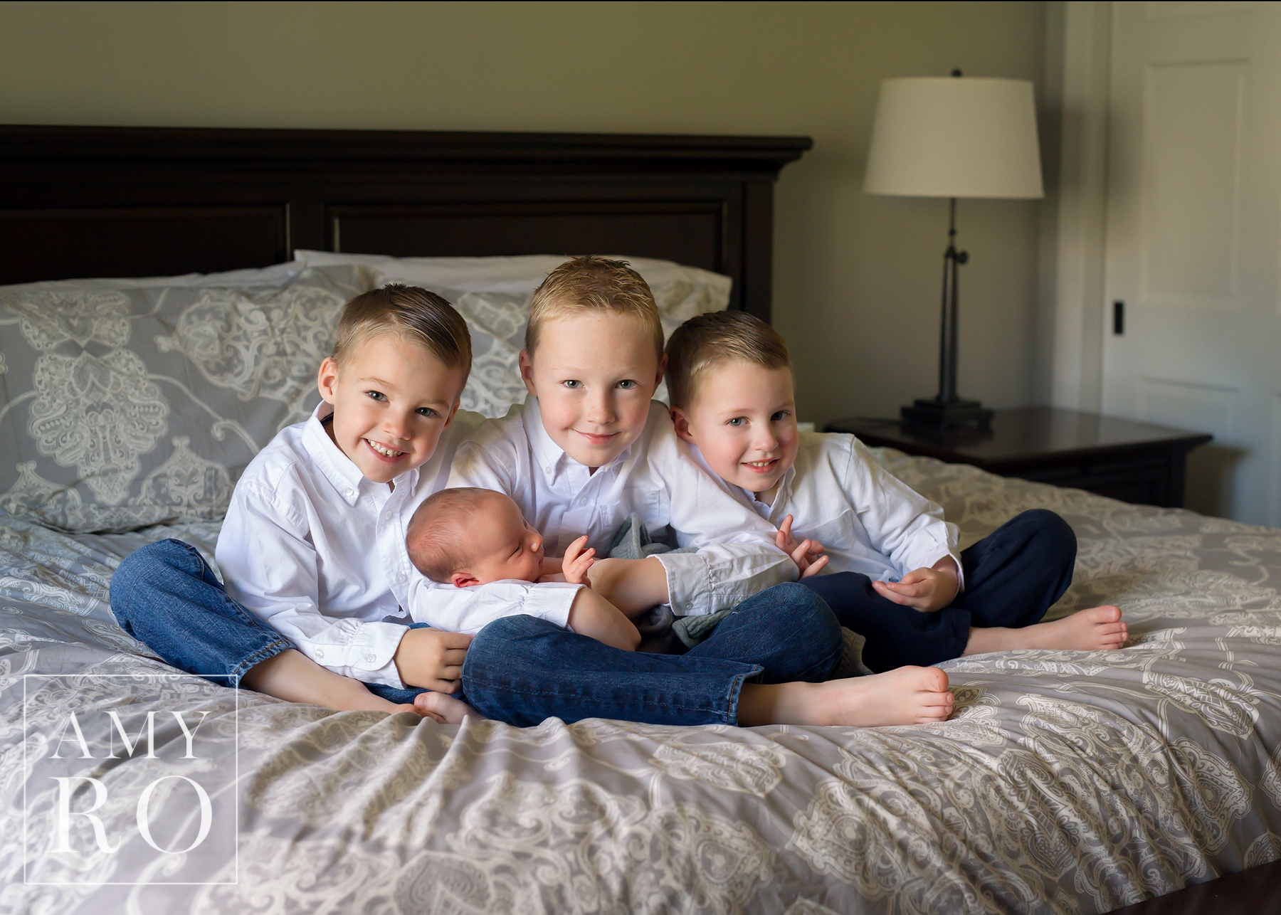 Three brothers snuggling their new baby brother on their parents bed during a lifestyle newborn session in Rhode Island