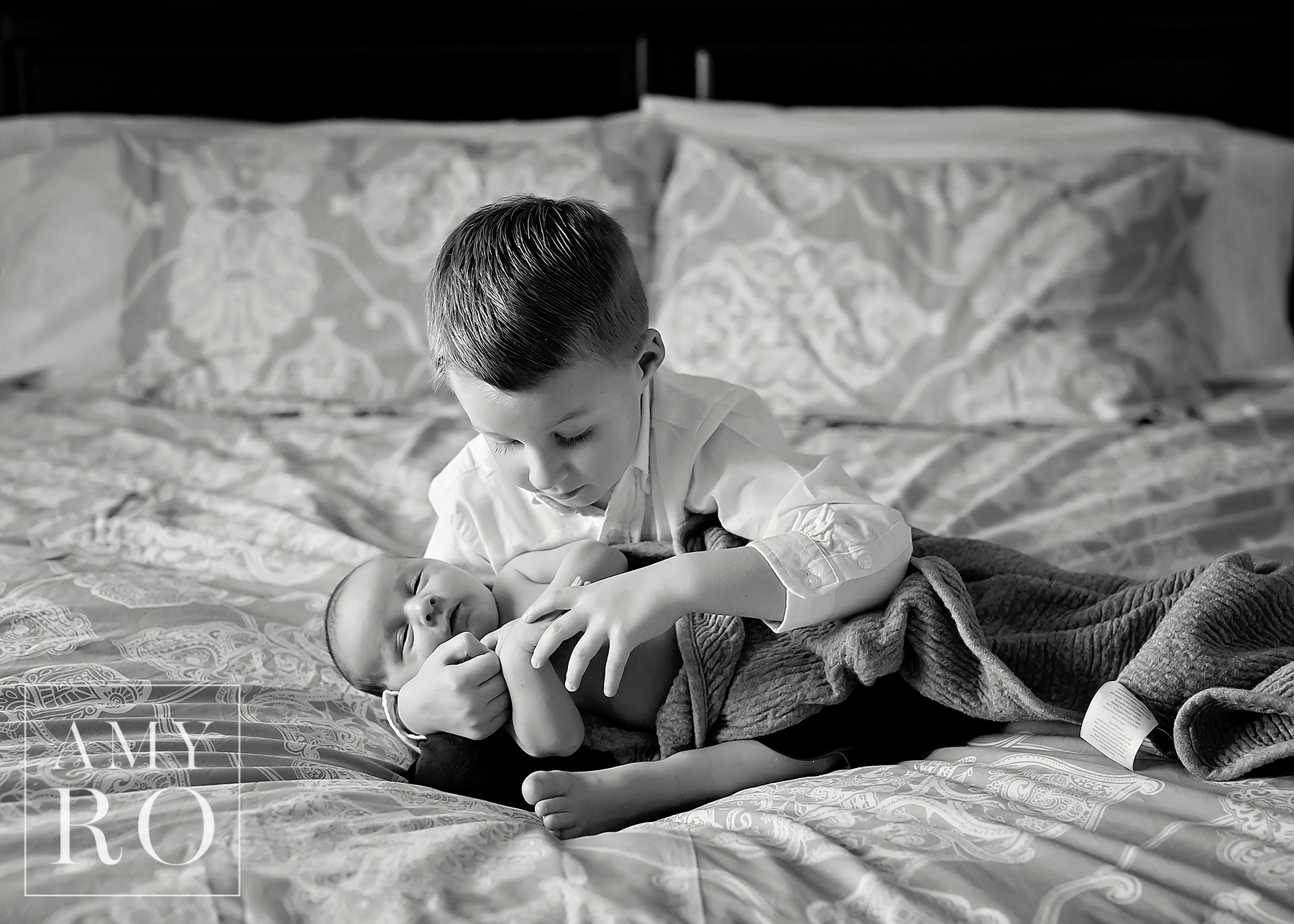 New big brother snuggling newborn baby on bed during a newborn session in Rhode Island