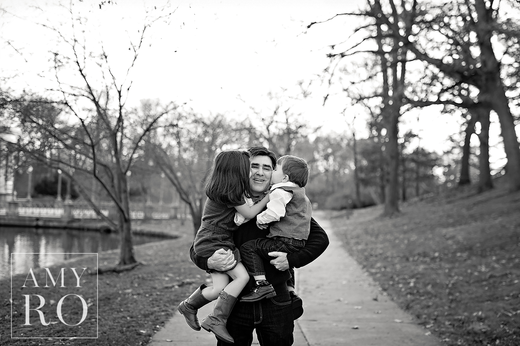 Black and white image of dad getting kissed by two kids during lifestyle family photograph session in Rhode Island