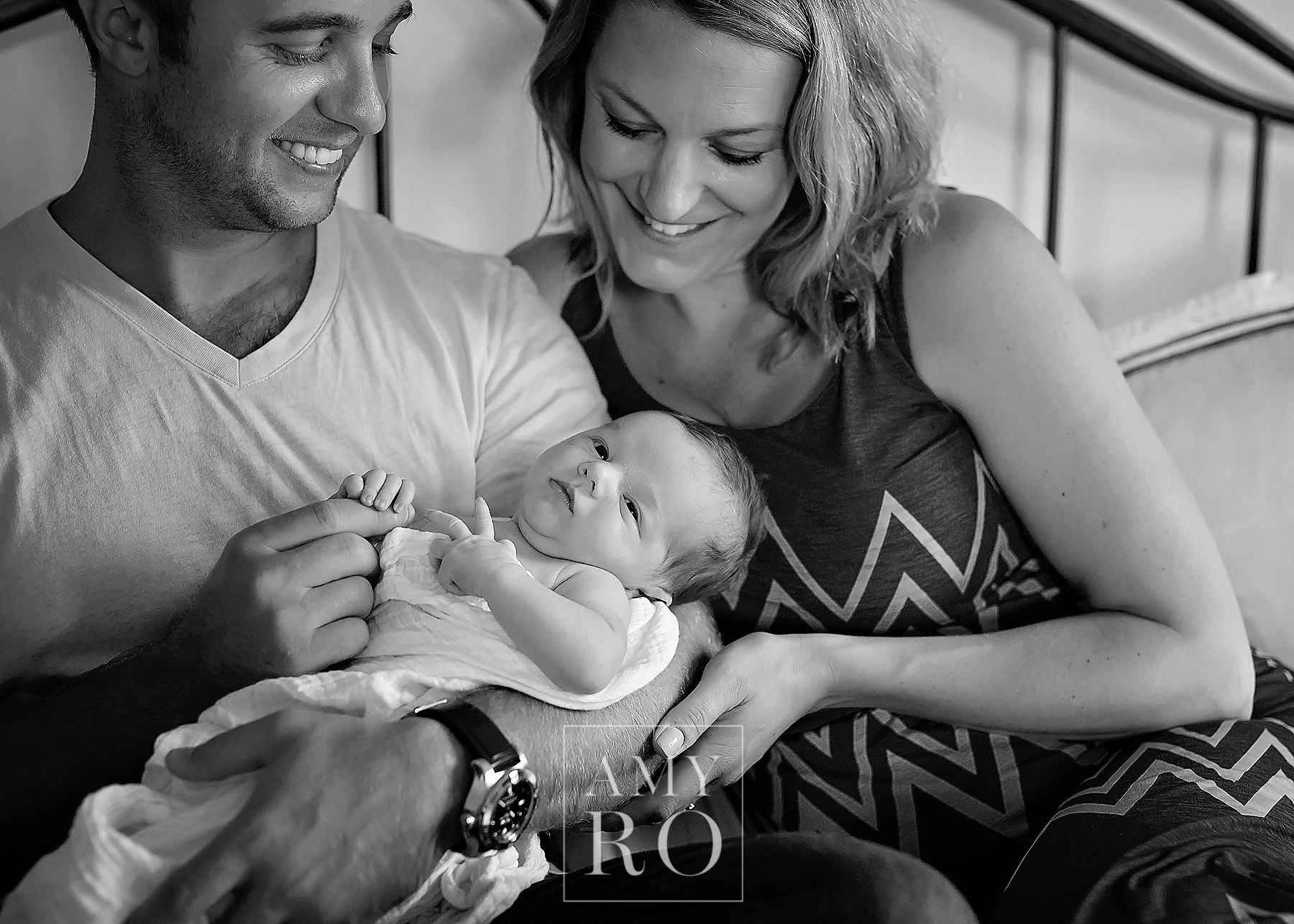 Black and white image of mom and dad with newborn son on bed suring an in home newborn lifestyle session in Massachusetts