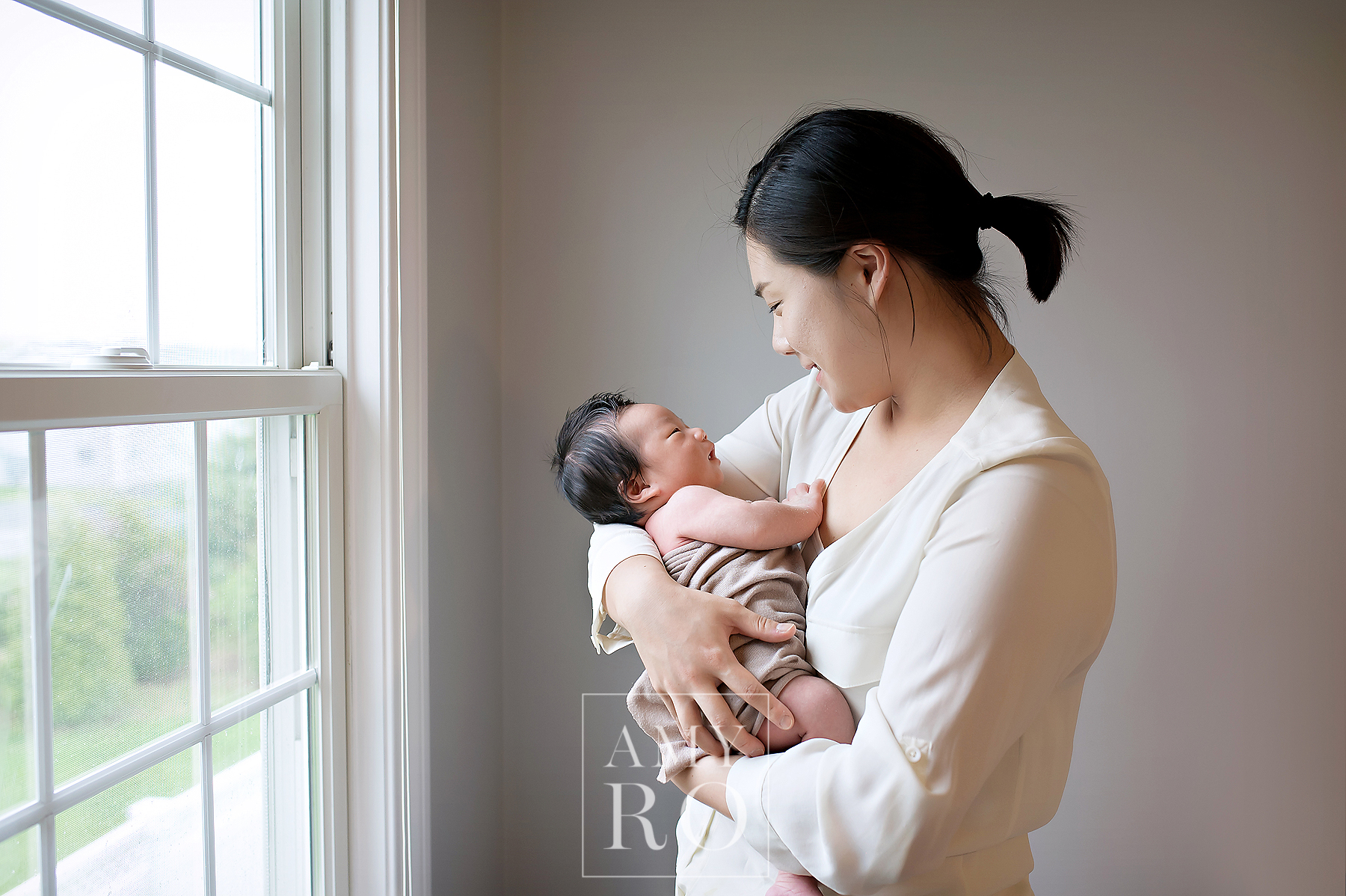 Image of mom and newborn son standing by a window during an in home lifestyle newborn session in Massachusetts