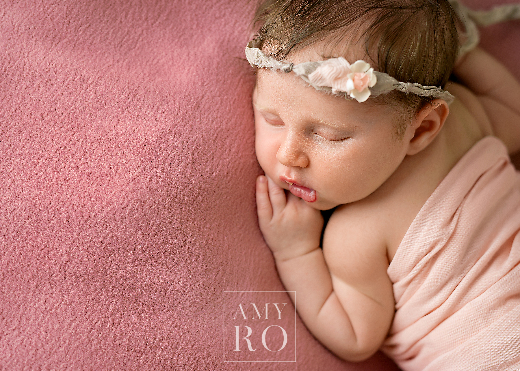 Color image of newborn baby girl profile in headband on pink blanket