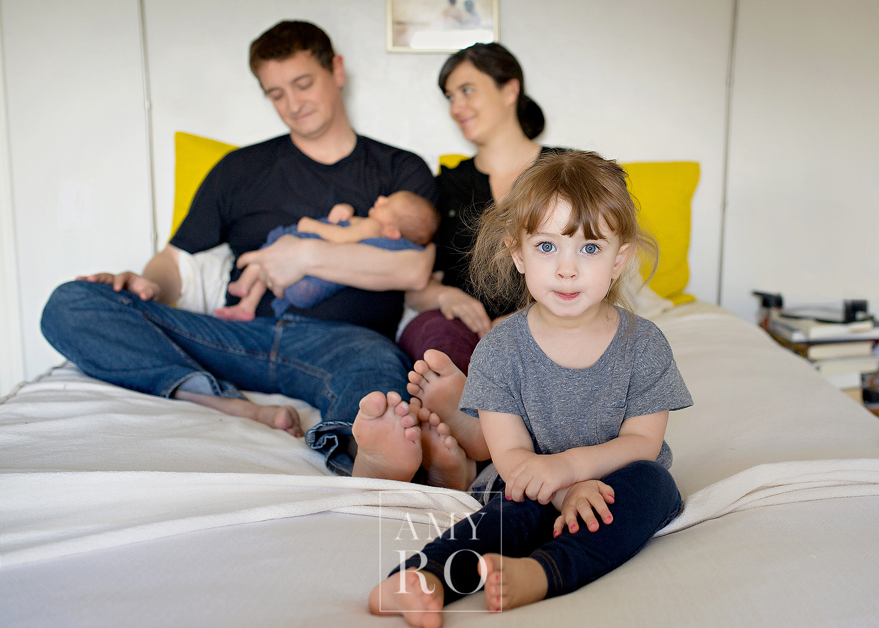 Image of family on bed with older sister during in home lifestyle newborn session in Massachusetts