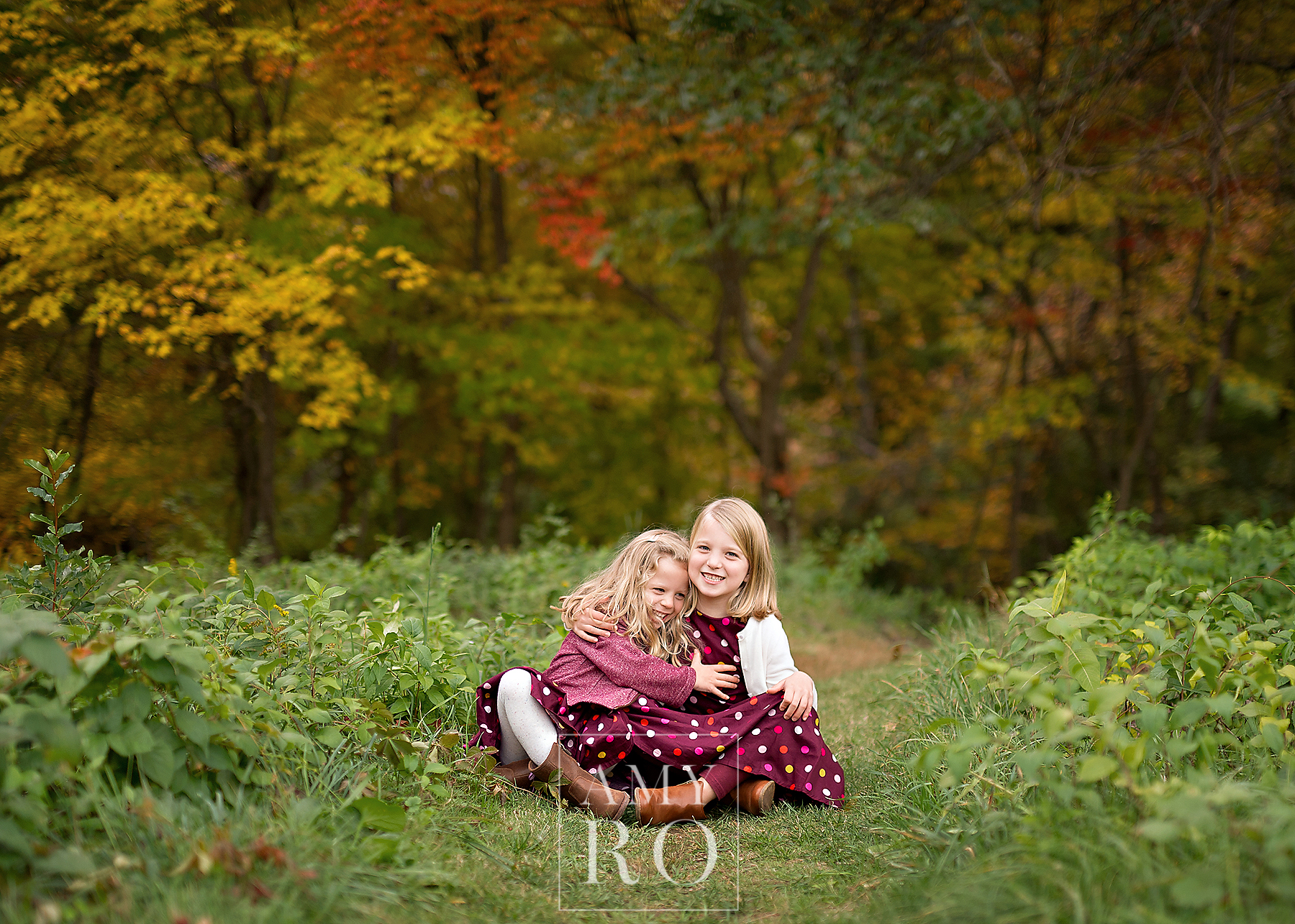 Fall holiday image of two sisters sitting hugging in the woods during a family photography session in Massachusetts