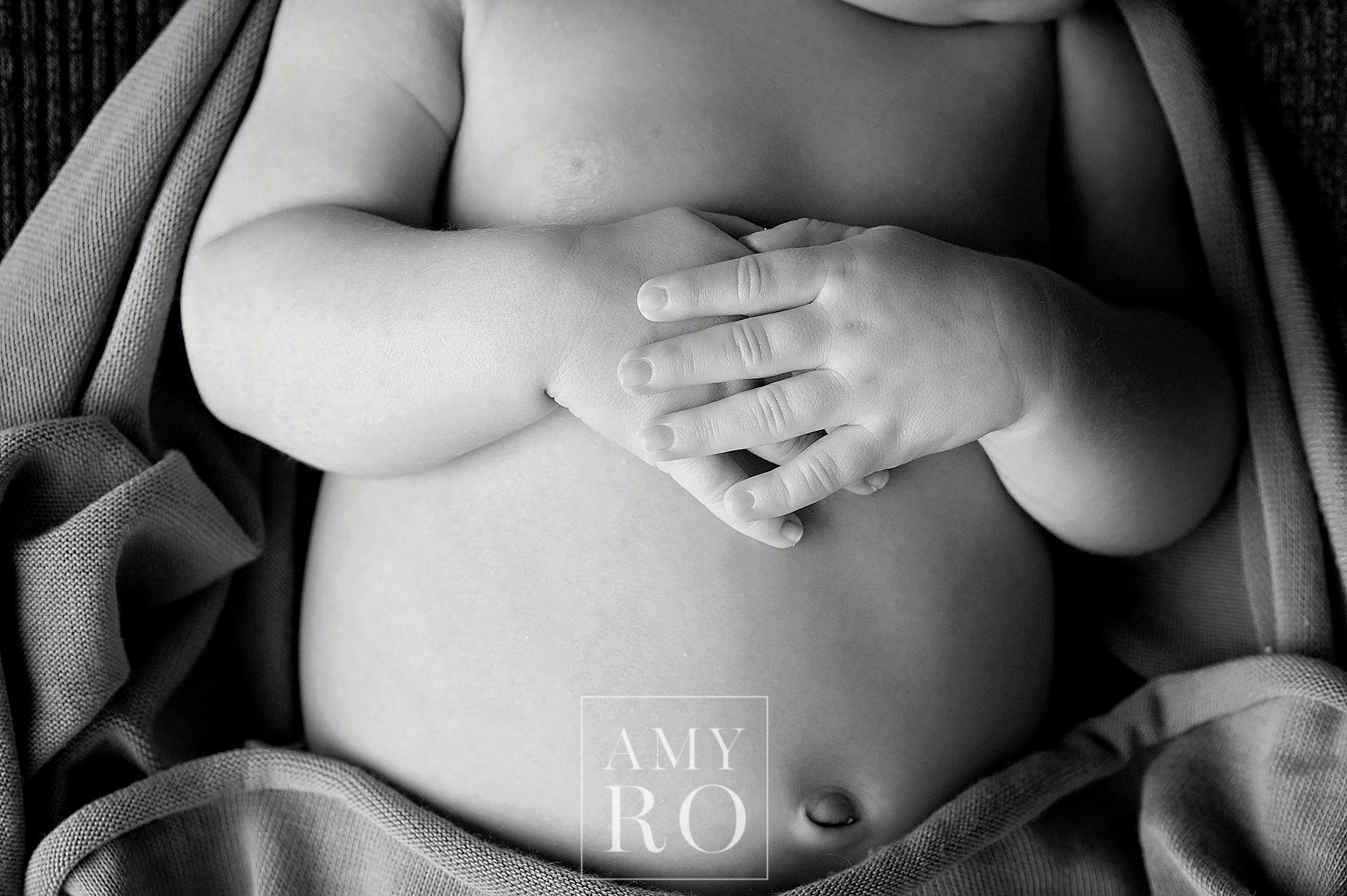 Black and white close up image of newborn hands folded on stomach