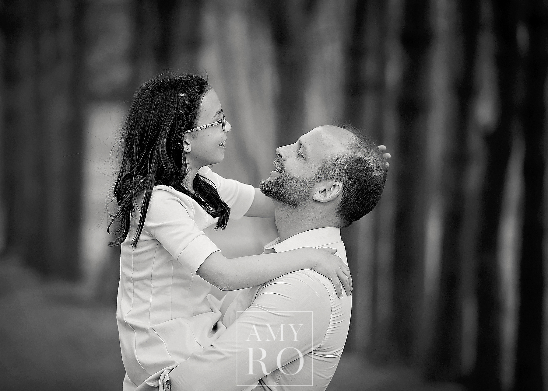 Black and white image of dad holding his older daughter laughing in the woods