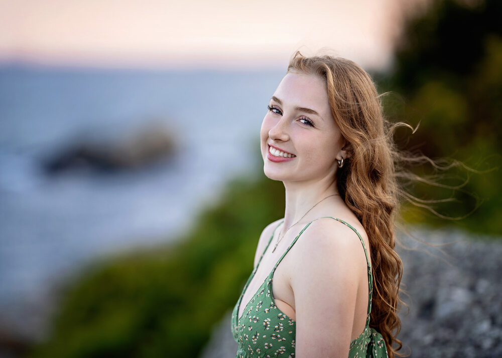 Senior girl in green spaghetti strap dress in front of the ocean in Rhode Island