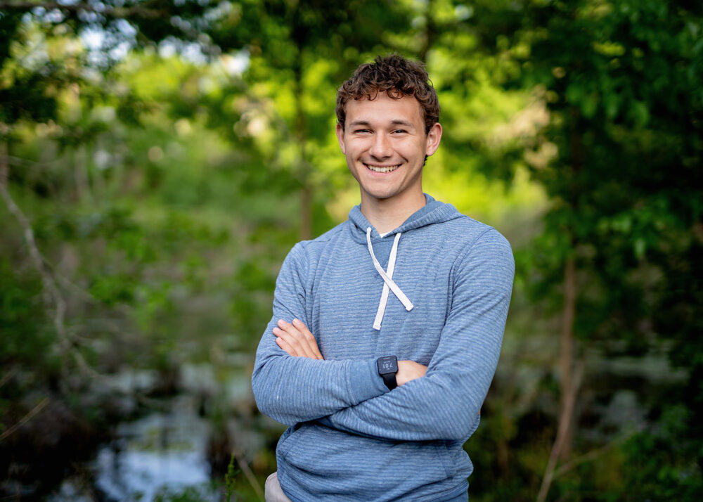 Arms crossed senior boy pose in front of water and trees in Cumberland Rhode Island