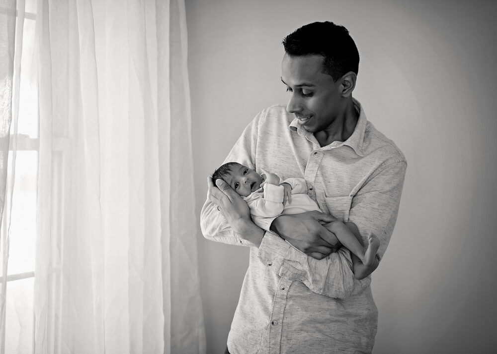 Dad in front of window with newborn in Lincoln Rhode Island