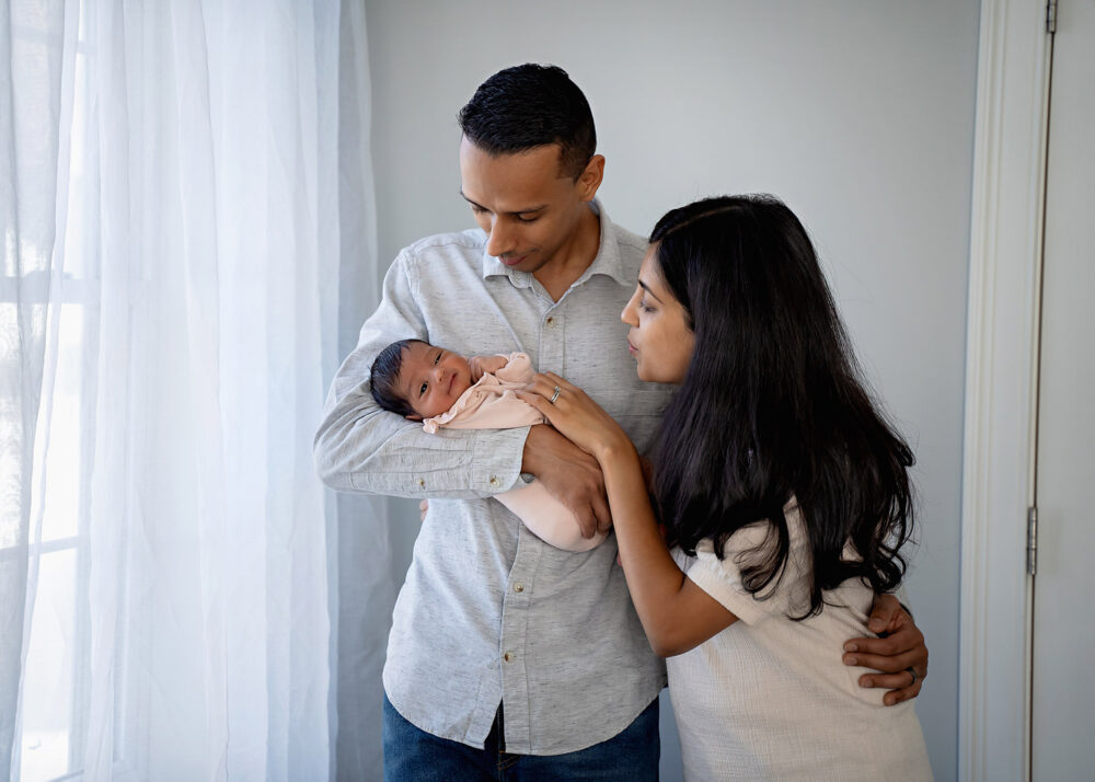 Mom and dad against window with newborn in Cumberland RI