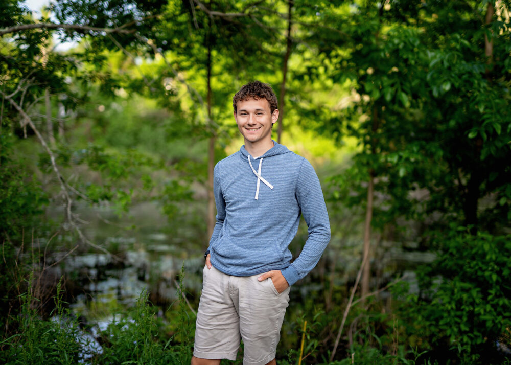 Senior boy in the Spring surrounded by trees and grass near Wrentham Massachusetts