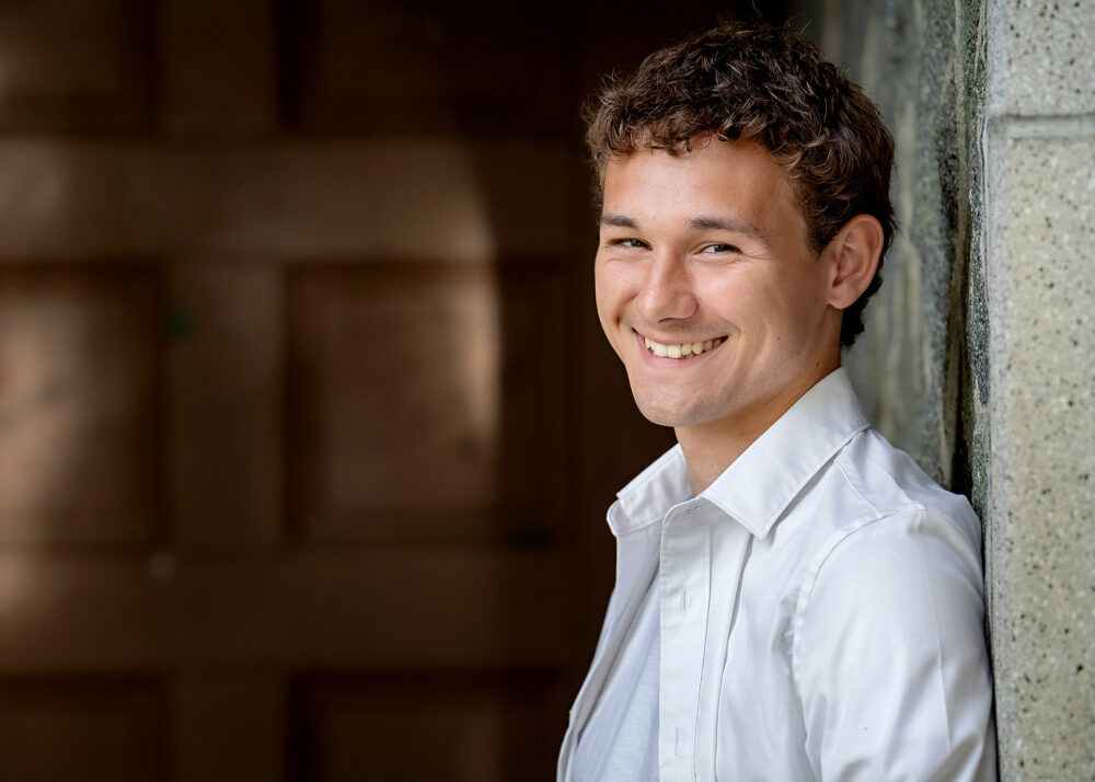 Smiling senior boy in front of door during session near North Attleboro Massachusetts