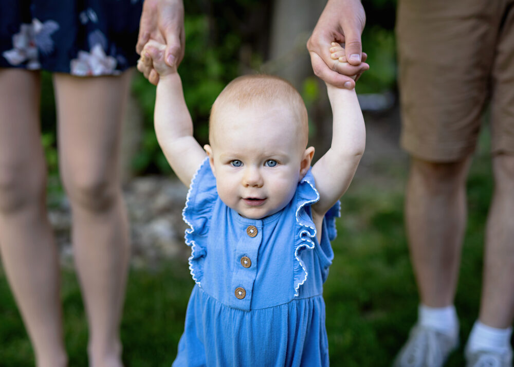 Baby holding mom and dads hands during family session in Providence RI