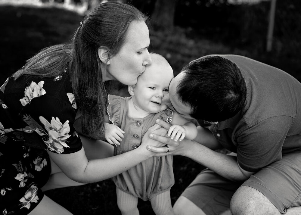 Mom and dad kissing baby during family photos near Lincoln RI