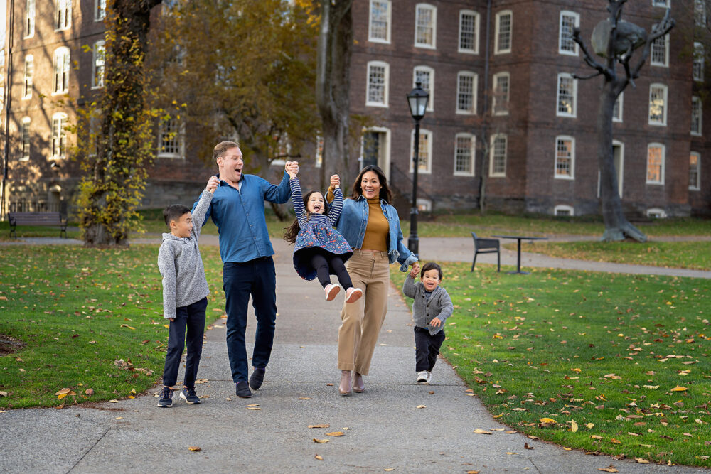 Mom and dad swinging youngest kid during lifestyle family session on campus Brown University