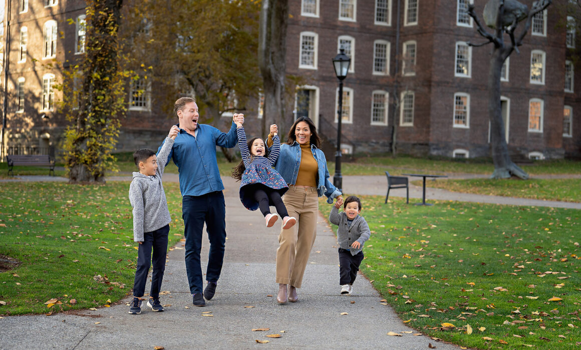 Mom and dad swinging youngest kid during lifestyle family session on campus Brown University