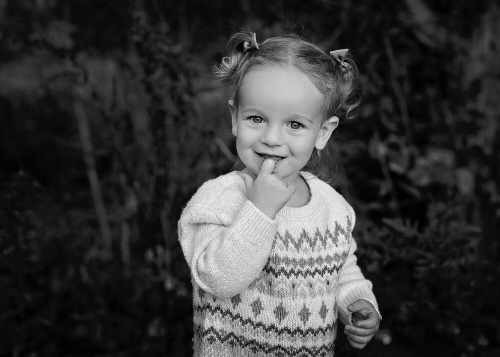 Toddler girl smiling with hand in mouth during fall photos in Rhode Island