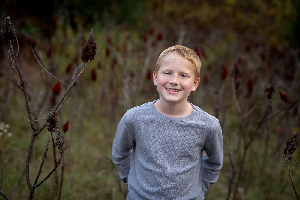 Young boy posing in tall grasses during family photos in Westborough Massachusetts